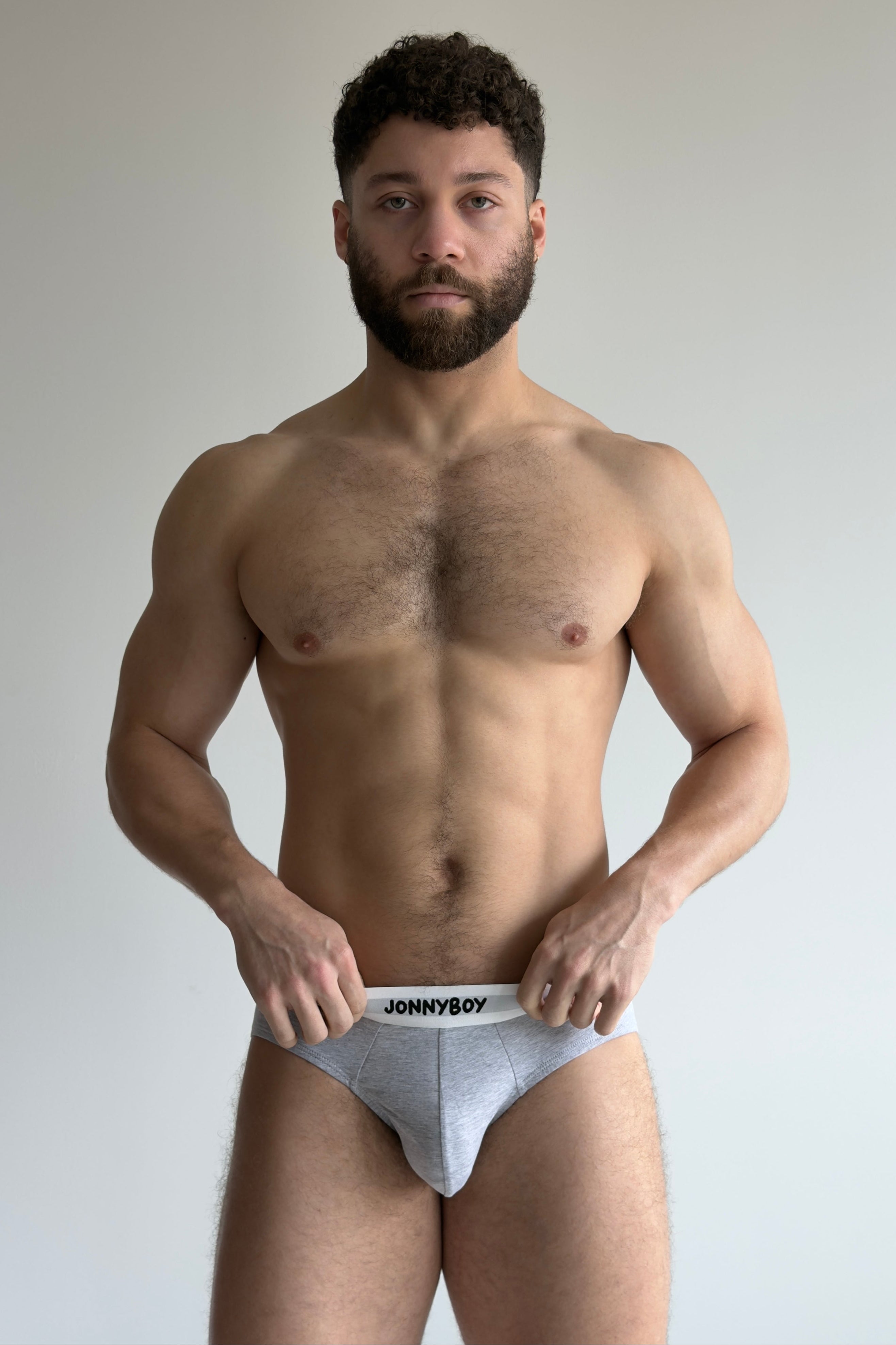Man holding a pair of underwear with 'Johnny Boy' branding against a plain background